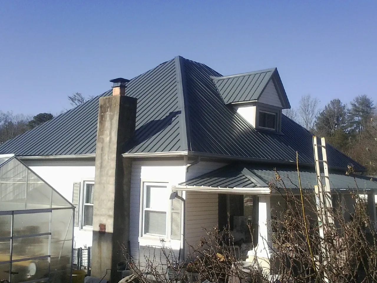 Dark blue standing seam metal roof on a white farmhouse with dormer — Slate & Tile Roof Repair by Roofing Brothers in Pittsboro