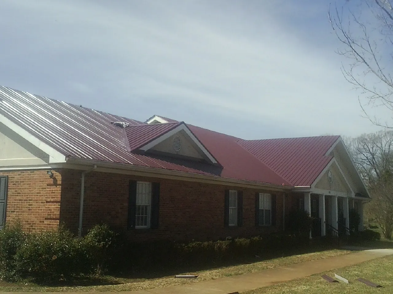 Red metal roof with gabled entries on a long brick building, from a Hail Damage Roof Repair job in Pittsboro