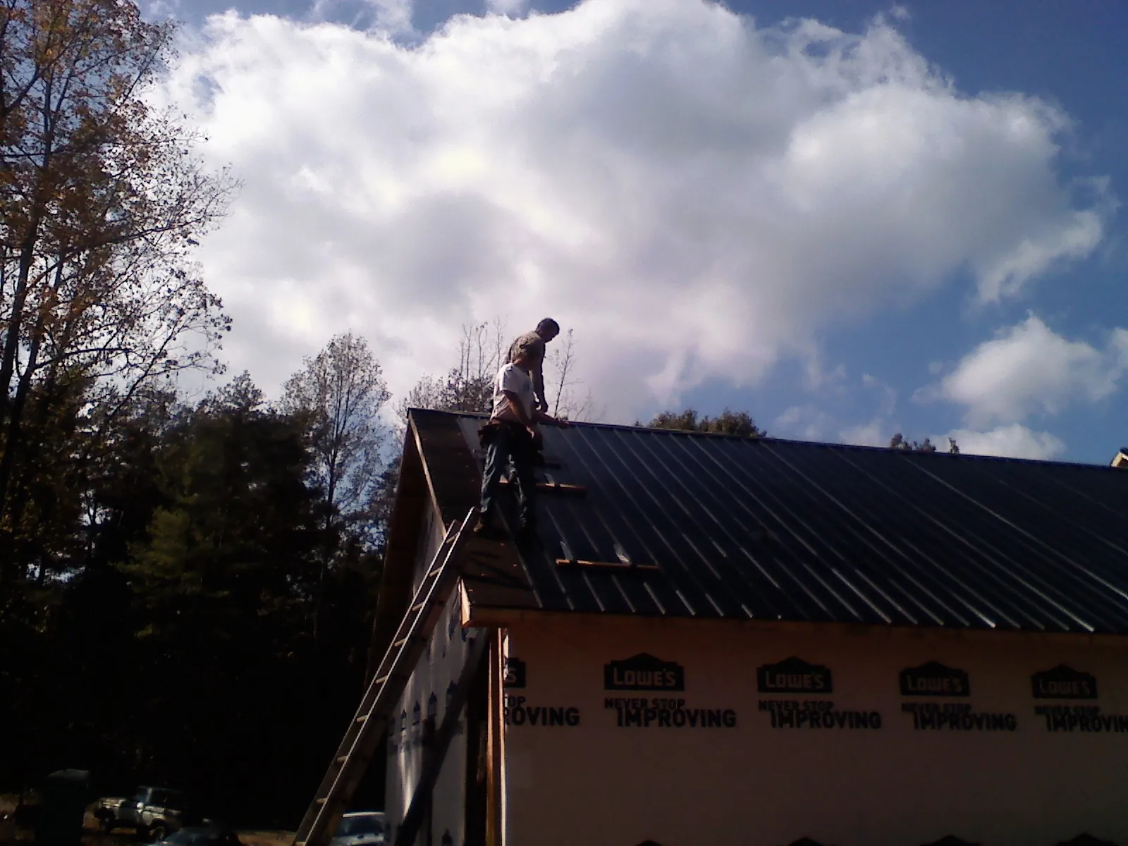 Roofer fastening dark metal panels high against a cloudy sky, from a Roof Inspection job in Pittsboro