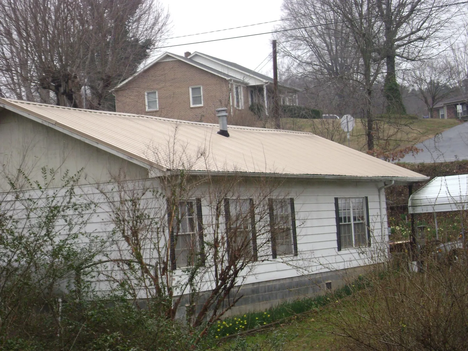 Tan metal roof on a white sided house set into a hillside — Commercial Roofing by Roofing Brothers in Pittsboro