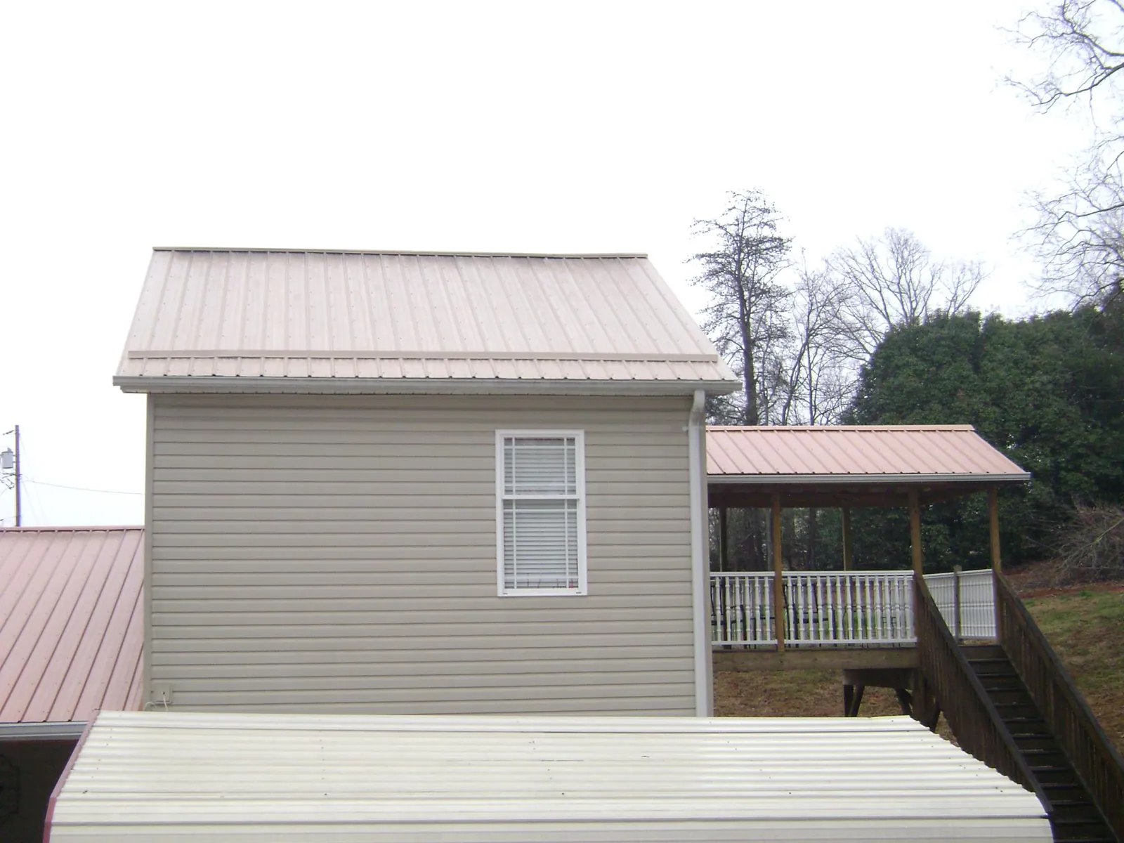 Tan metal roofs on a two story addition and attached porch, from a Roof Replacement job in Pittsboro